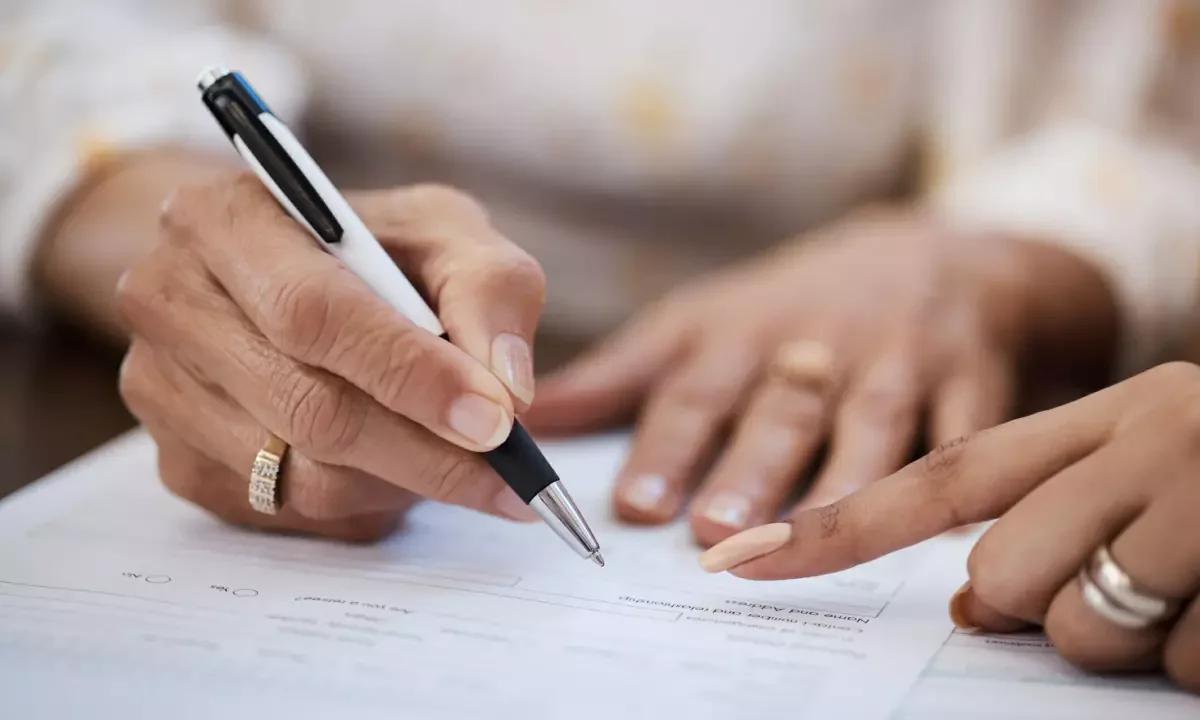 Gros plan sur une personne qui signe un formulaire, accompagnée d’un conseiller, pour demander le déblocage de son épargne retraite PER