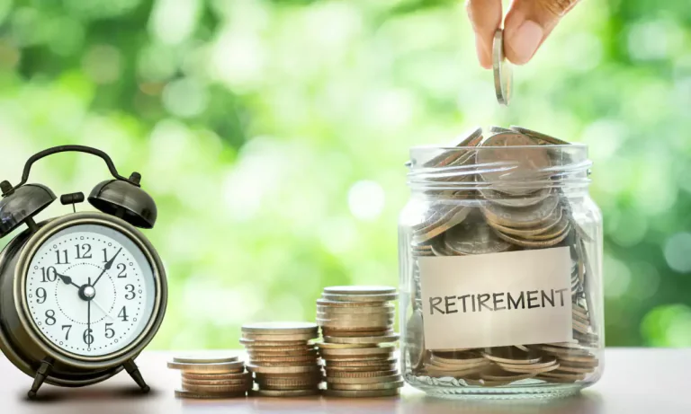 Bocal rempli de pièces étiqueté « retirement » à côté d’un réveil, symbolisant l’épargne retraite PER et la fiscalité dans le temps