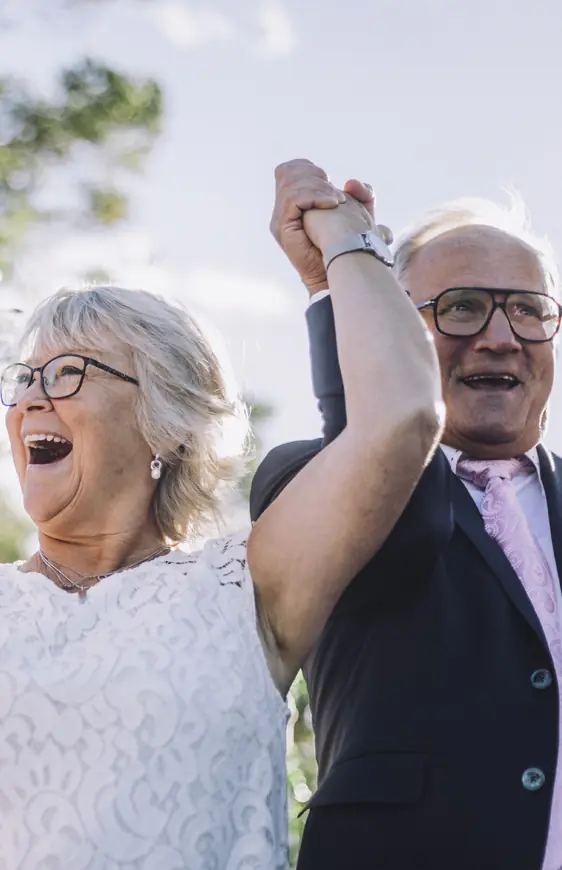 Couple de seniors souriants levant les bras en extérieur, célébrant une retraite sereine