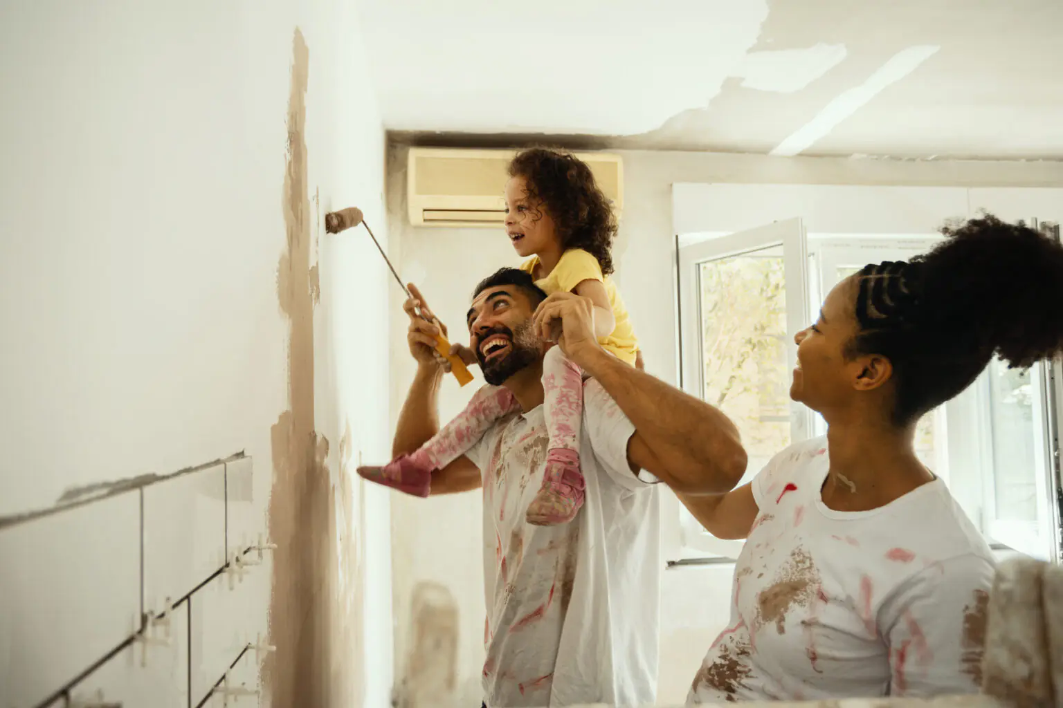 Parents et enfant repeignant un mur ensemble, illustrant un projet de vie familiale