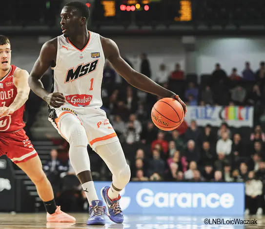 ©LNB/LoicWacziak Joueur de basket en action sur un parquet, avec présence du logo Garance en arrière-plan