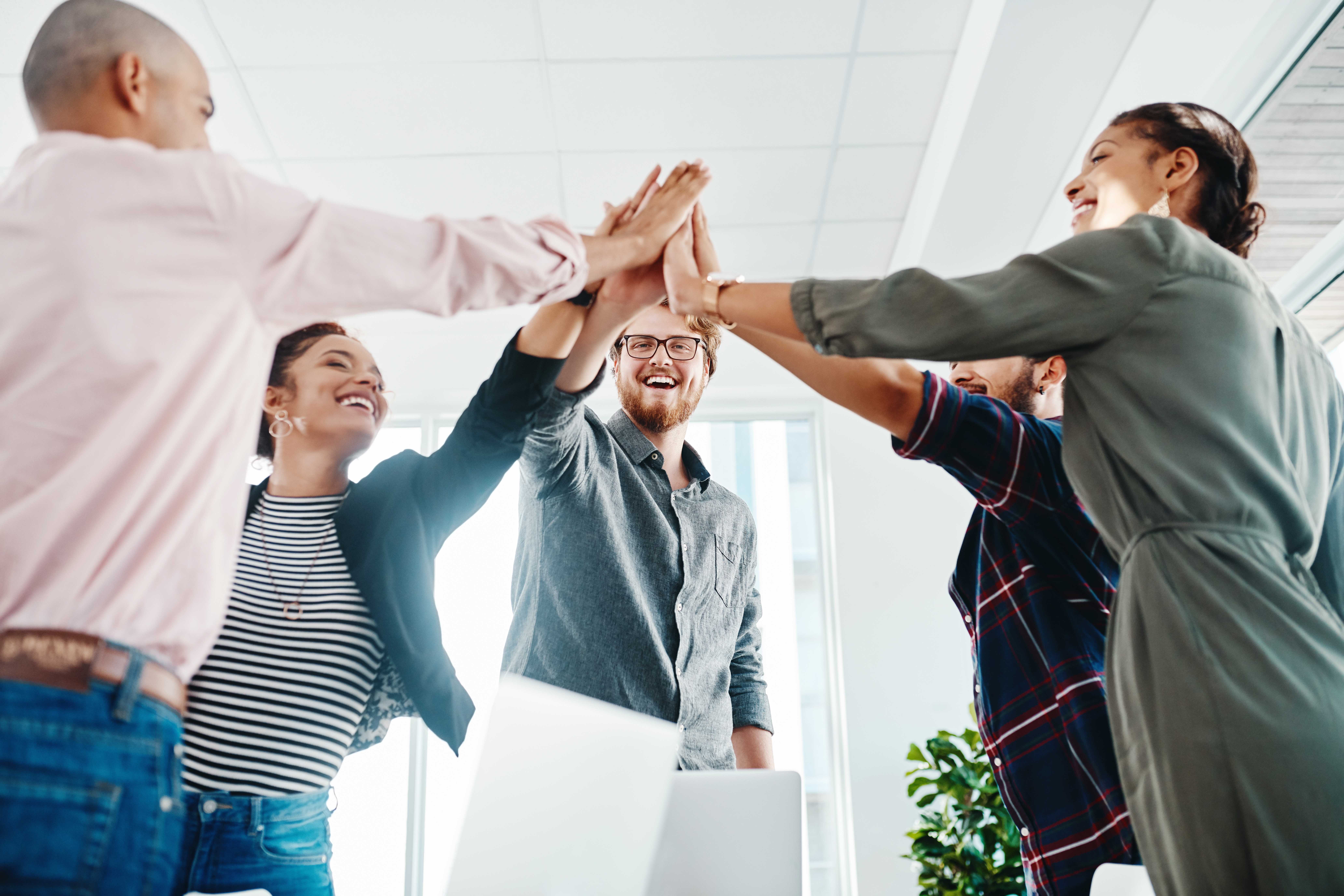 Groupe de collègues célébrant avec un high five collectif dans un bureau lumineux.