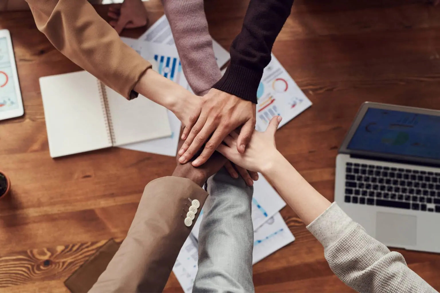 Plusieurs mains empilées au-dessus de documents et d’un ordinateur portable, symbole d’un engagement commun