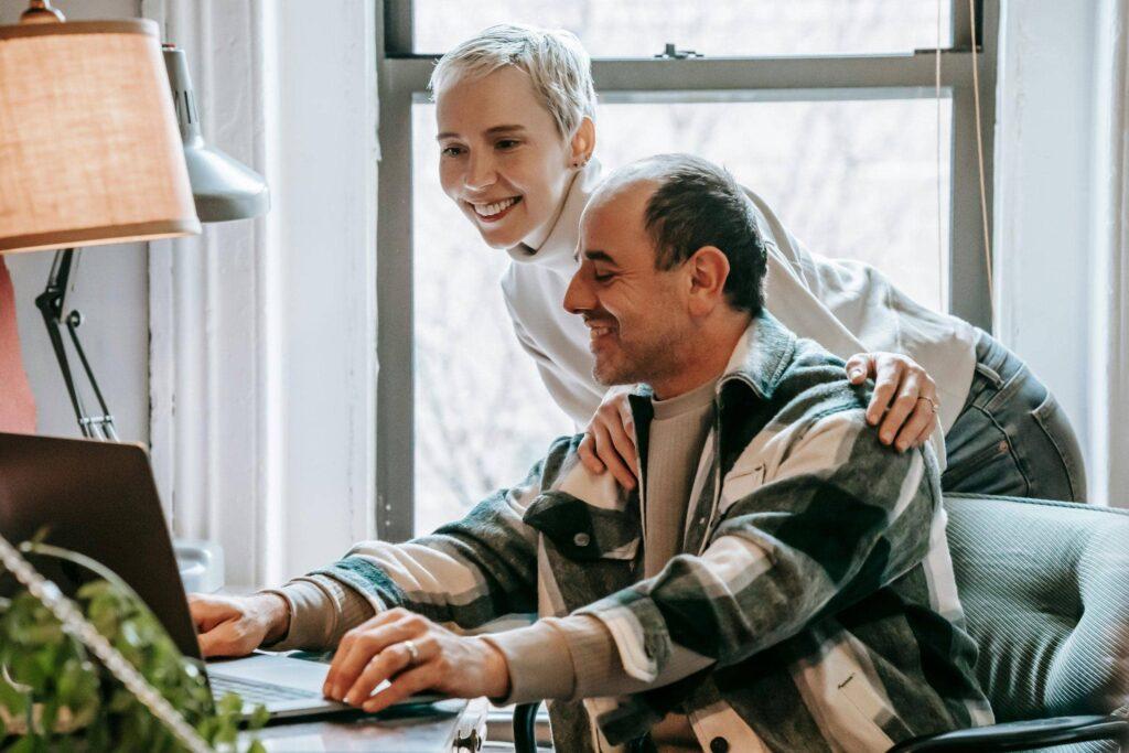 Couple souriant consultant un ordinateur à domicile, représentant la planification et l’anticipation financière avec Garance