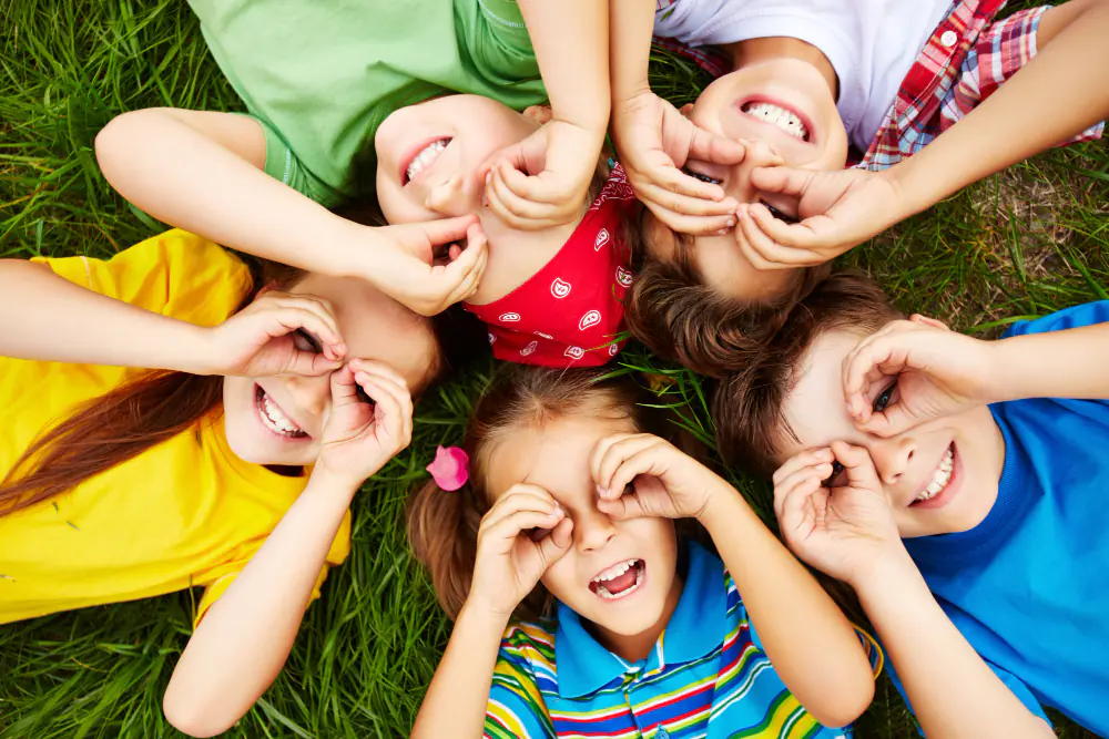 Groupe d’enfants allongés dans l’herbe en train de jouer et de rire, illustration de l’avenir et des projets d’enfance.