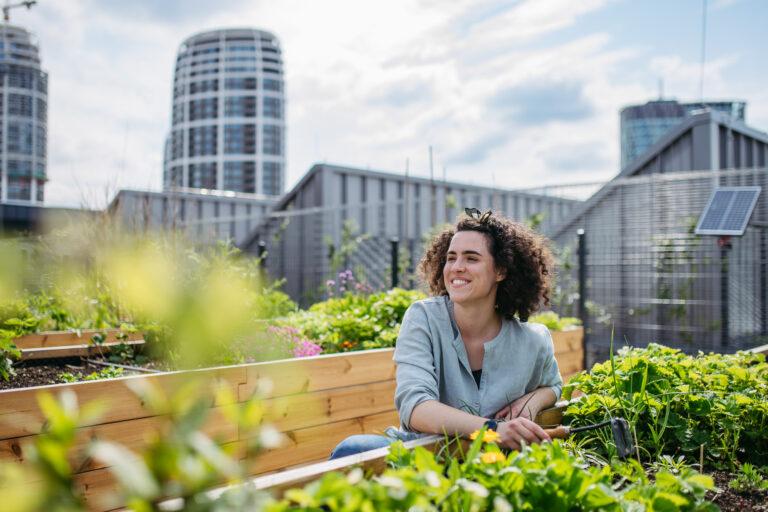 Femme souriante dans un potager urbain sur un toit avec immeubles en arrière-plan