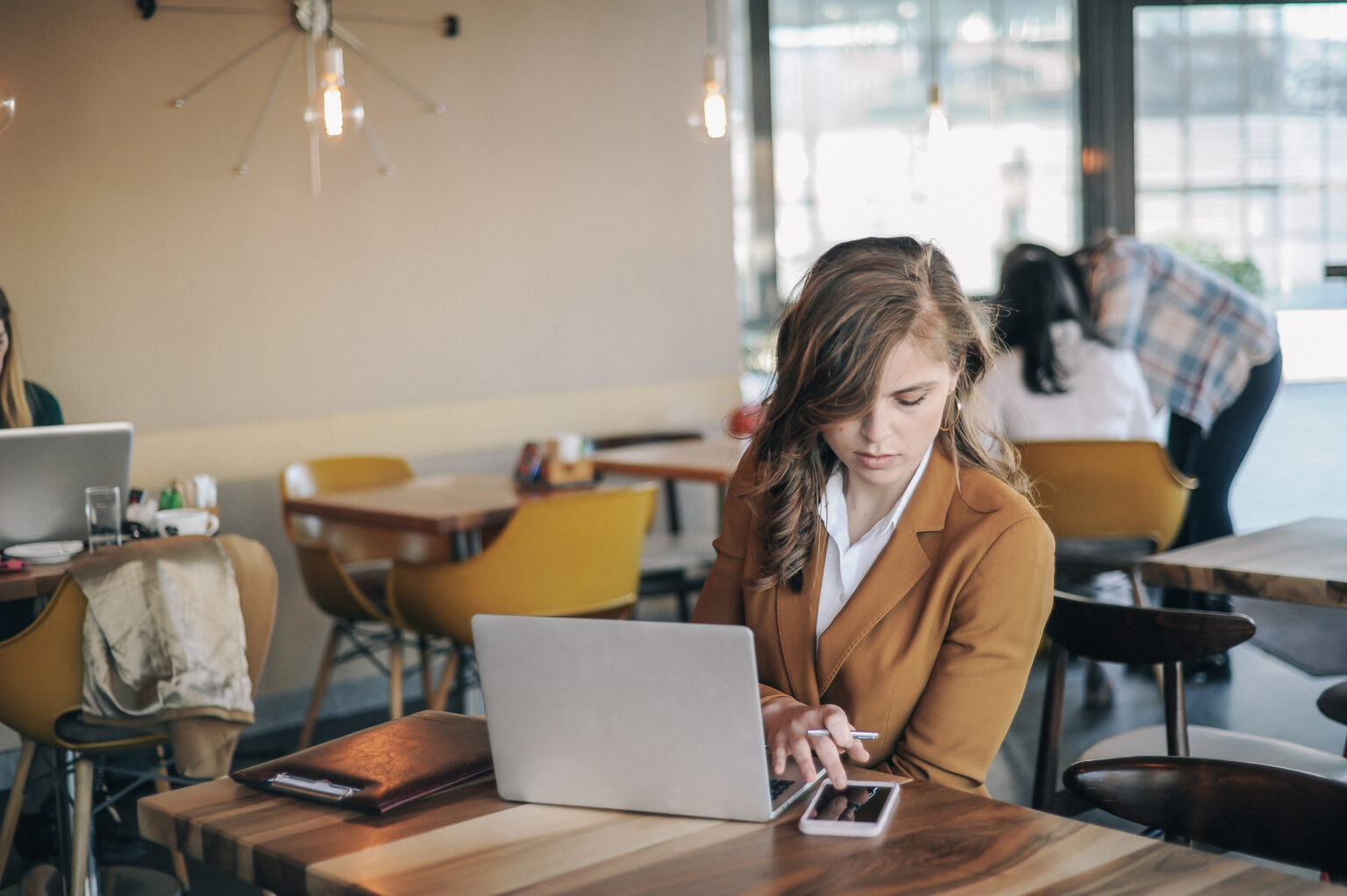 Jeune femme travaillant dans un café, sur son ordinateur et son téléphone
